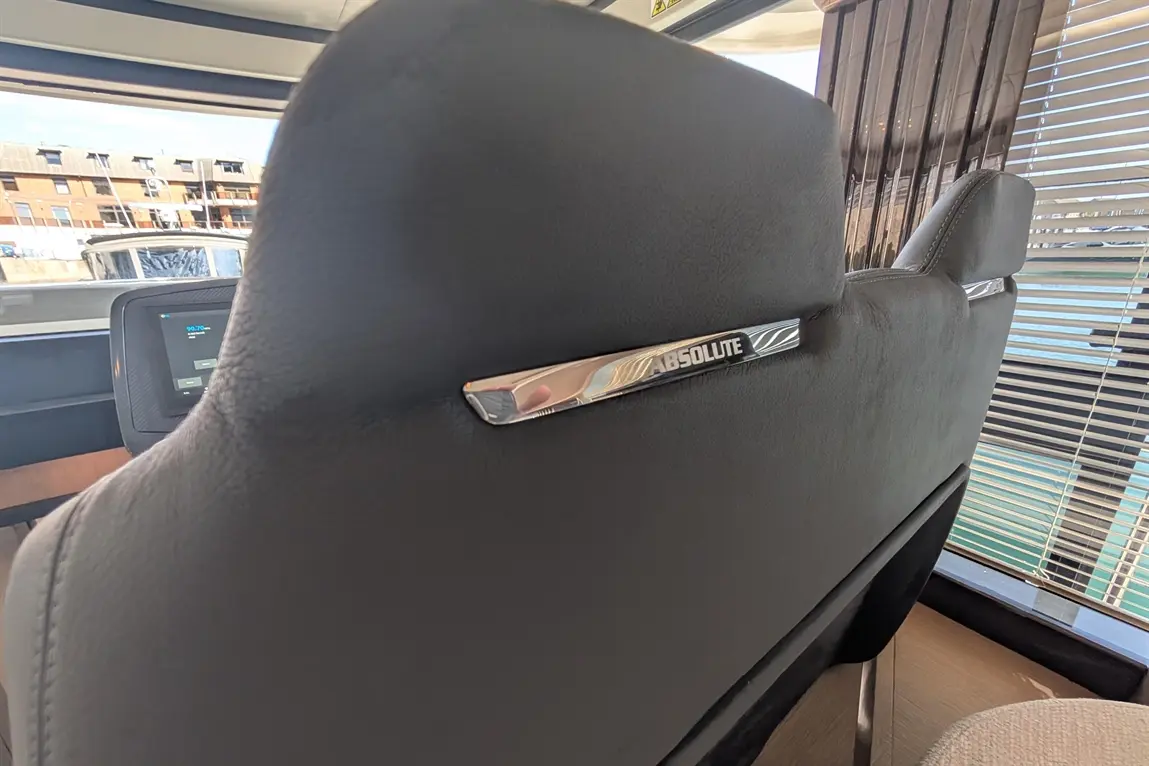 Black leather seat with a metallic "ABSOLUTE" label, facing a window with blinds and a glimpse of buildings outside.